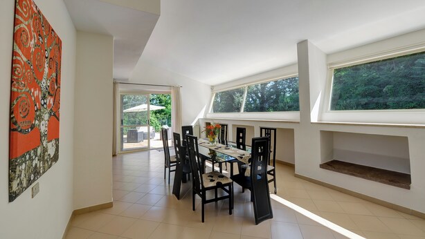 Uma área de refeições com mesa e cadeiras, uma janela grande e vista para o verde lá fora.