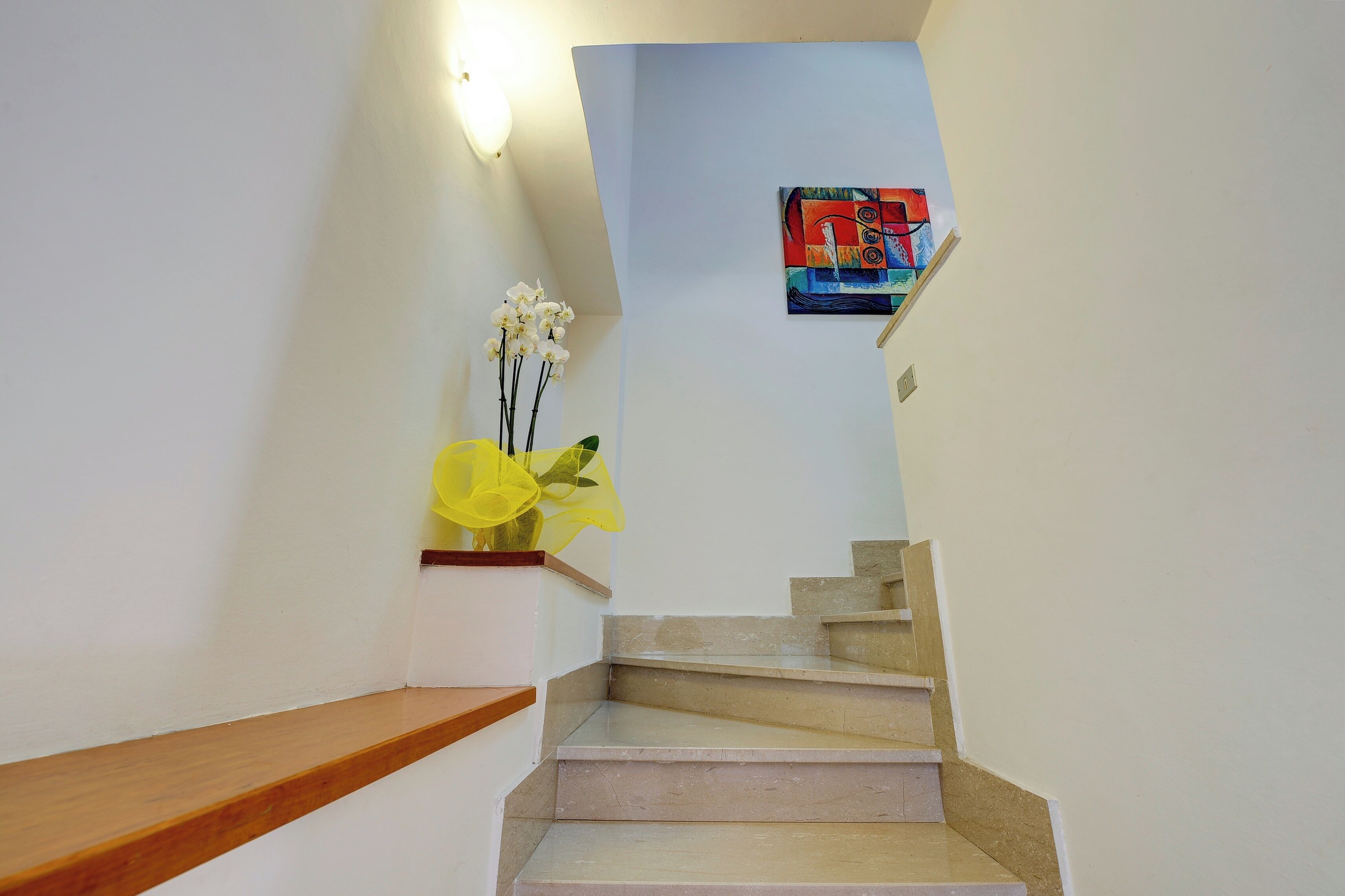 Un escalier avec une rampe en bois et un arrangement floral jaune accroché au mur.