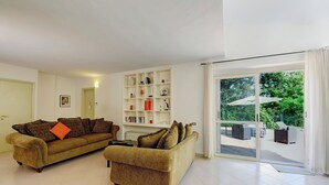 Sala de estar com dois sofás, uma estante de livros e uma porta de correr de vidro que dá para uma área externa.