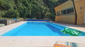 Une piscine avec un jouet gonflable vert, un mur de pierre et un bâtiment doté d’une fenêtre et d’une horloge.