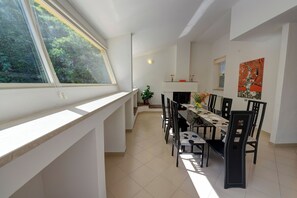 Un espace repas avec une table haute et des chaises, une fenêtre donnant sur un paysage verdoyant et un tableau accroché au mur.