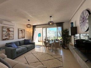 Uma sala de estar moderna com sofá, mesa de jantar, cadeiras, um relógio grande e vista para o exterior.