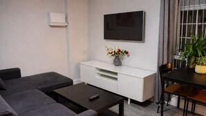 Una sala de estar con sofá, mesa de centro, televisor, mueble blanco y una mesa de comedor con sillas.