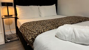 Una cama con colcha de estampado de leopardo, cabecera negra, almohadas blancas y una lámpara de noche.