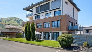 A modern two-story building with a balcony, large windows, and a well-maintained lawn.
