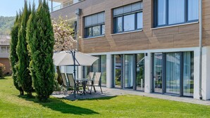 A modern building with a patio area, outdoor seating, and tall trees.