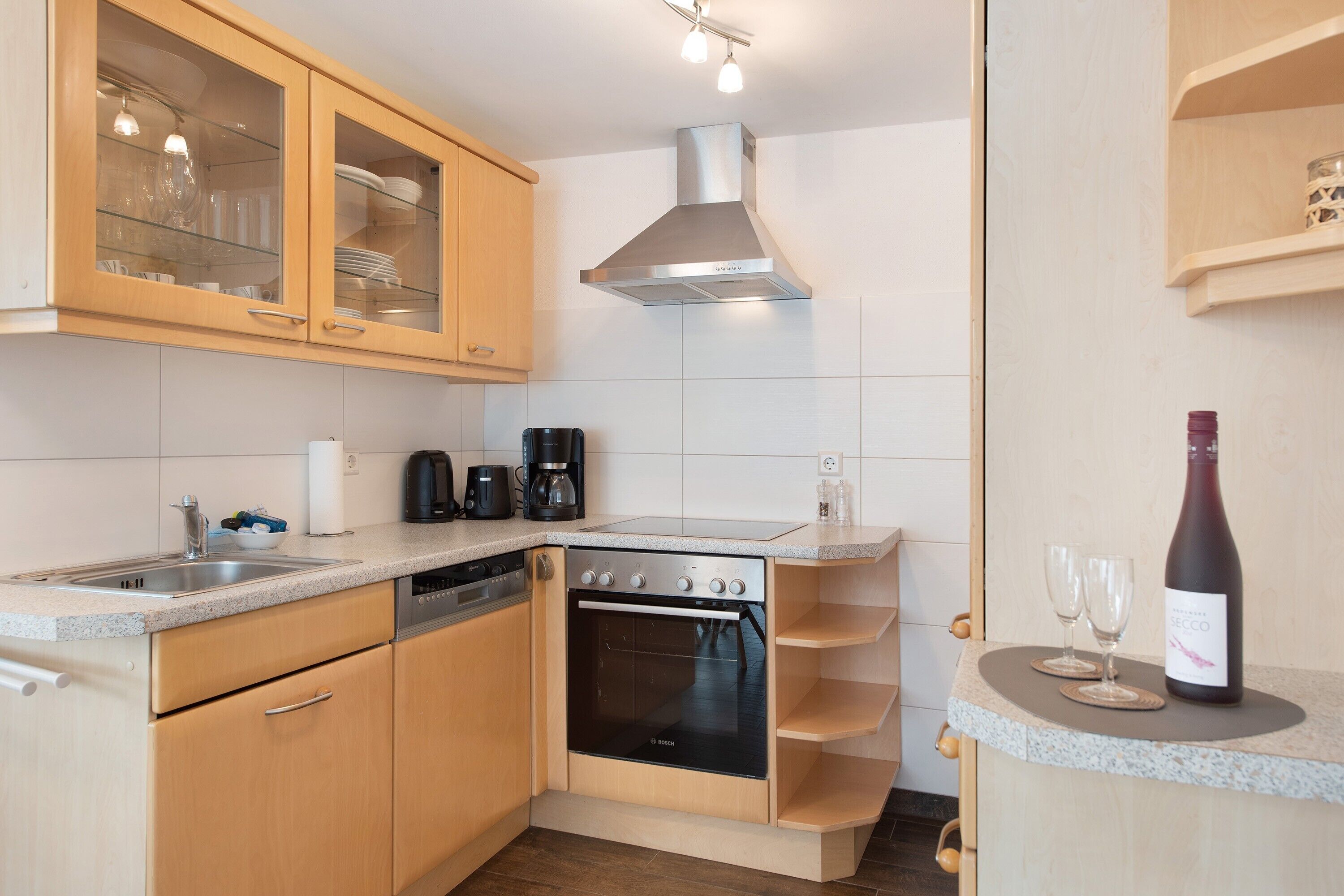 A kitchen with wooden cabinets, a Bosch oven, a coffee maker, and a wine bottle.