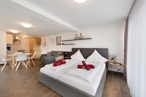A modern hotel room with a bed, bedside table, and a view of the kitchen area.