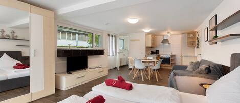 A modern hotel room with a bed, a sofa, a dining area, and a kitchen.
