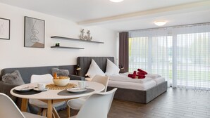 A modern living room with a sofa, a dining table, a bed, and artwork on the walls.