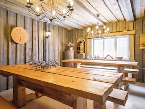 A rustic wooden dining area with a large table and benches, a chandelier, and a window with natural light.