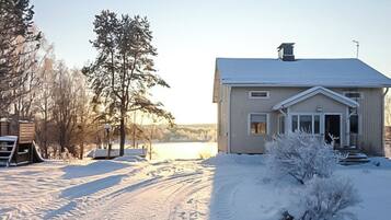 Een huis bedekt met sneeuw, met een heldere lucht, een pad dat naar de ingang leidt, en een kleine struik op de voorgrond.