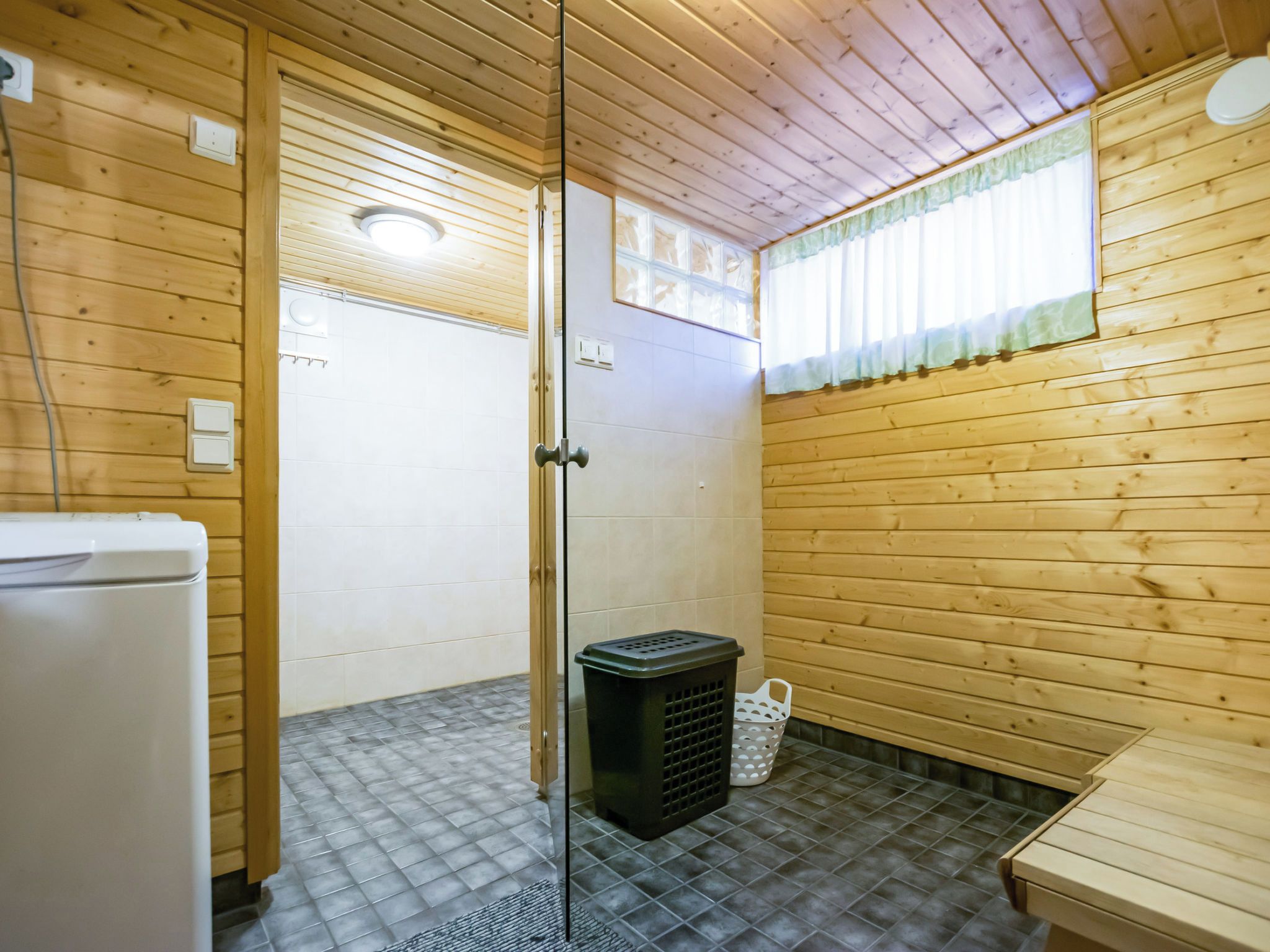 Een badkamer met houten lambrisering, een douche, een wit toilet en een klein wastafeltje.