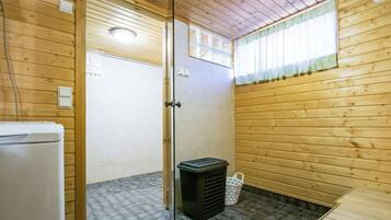 Een badkamer met houten lambrisering, een douche, een wit toilet en een klein wastafeltje.