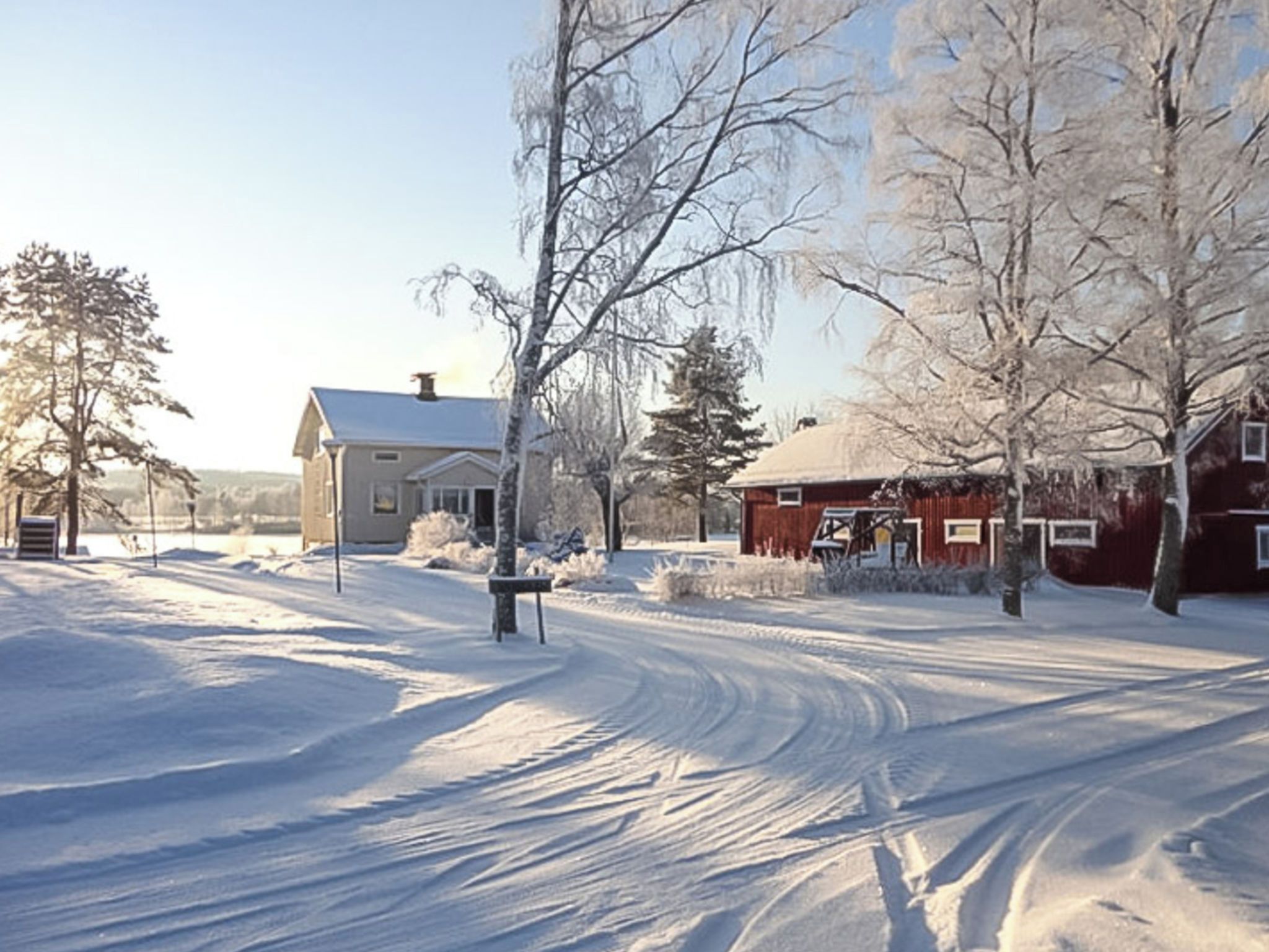 A snow-covered landscape with a house and a red barn.
