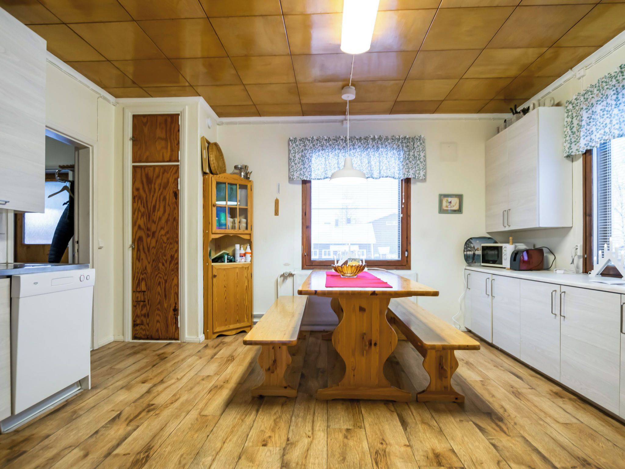 A kitchen with wooden cabinets, a wooden table, and a window with blinds.