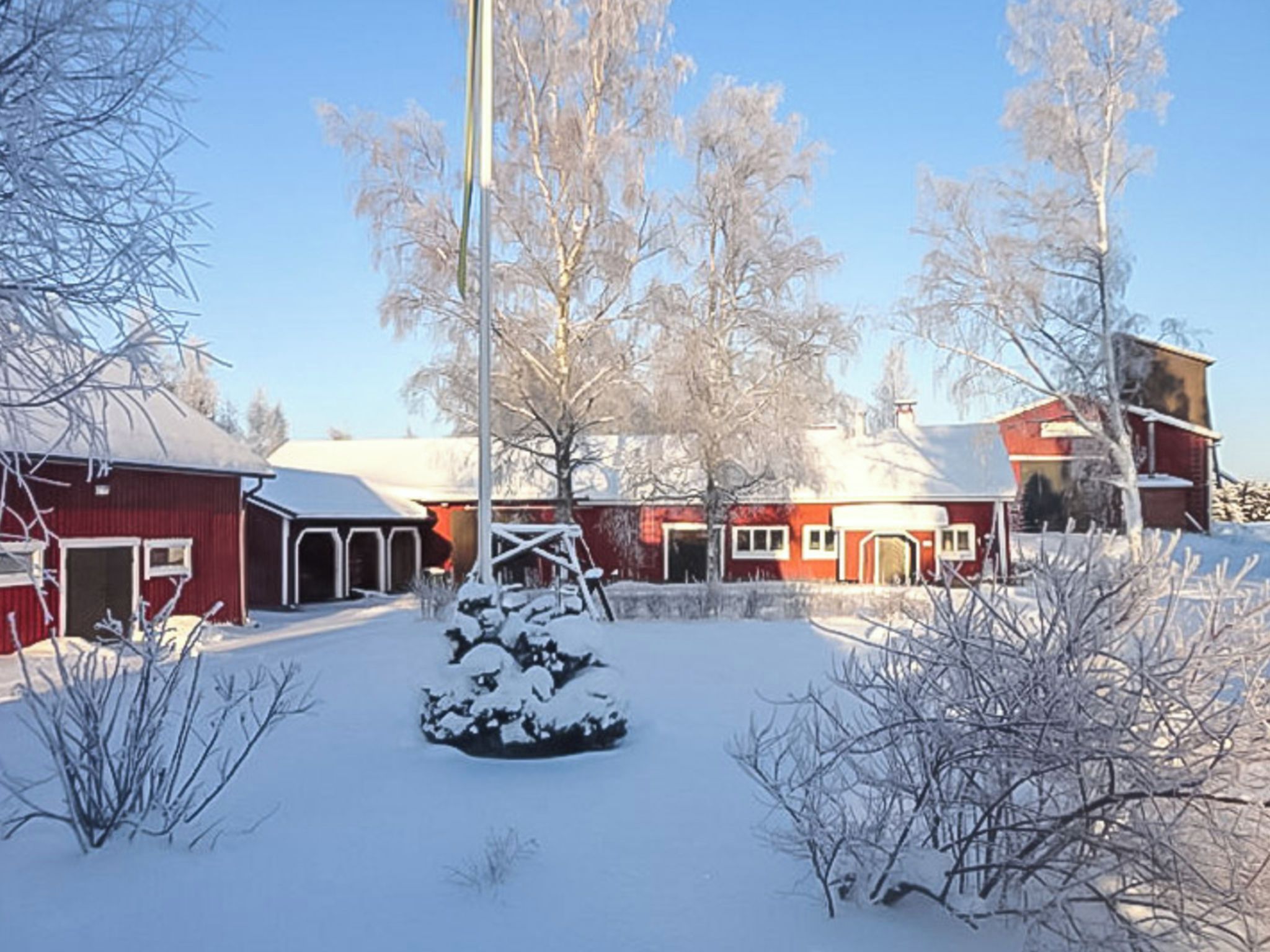 Ett snötäckt landskap med en röd ladugård och en träkonstruktion i förgrunden.