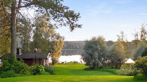A grassy field with a small red building and a large tree in the foreground. - Vacation home Jutila by Interhome (Jämijärvi)