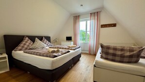 A bedroom with a bed, a bedside table, a chair, a window with curtains, and a radiator.