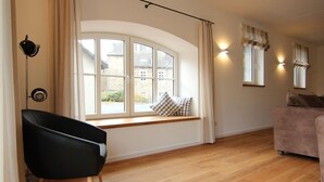 A room with a large window, a black chair, a sofa, and a lamp.