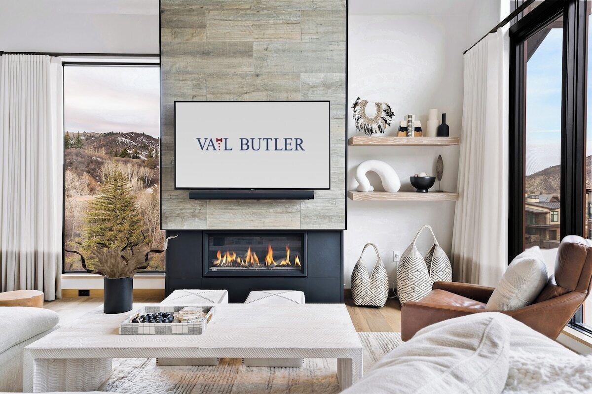 A modern living room with a fireplace, a television mounted above it, and a view of the outdoors.
