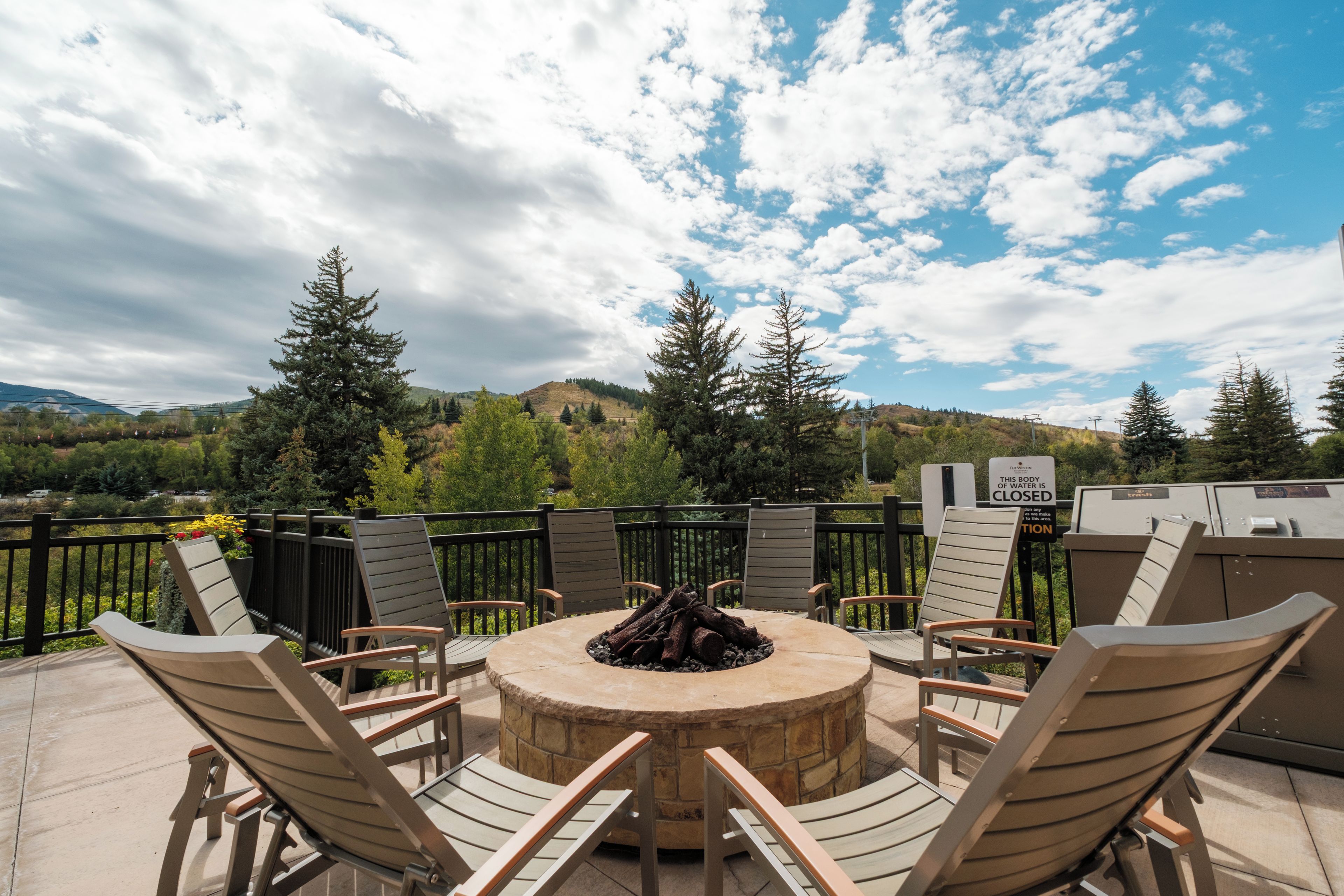 A patio with a stone fire pit surrounded by wooden chairs, overlooking a mountainous landscape.