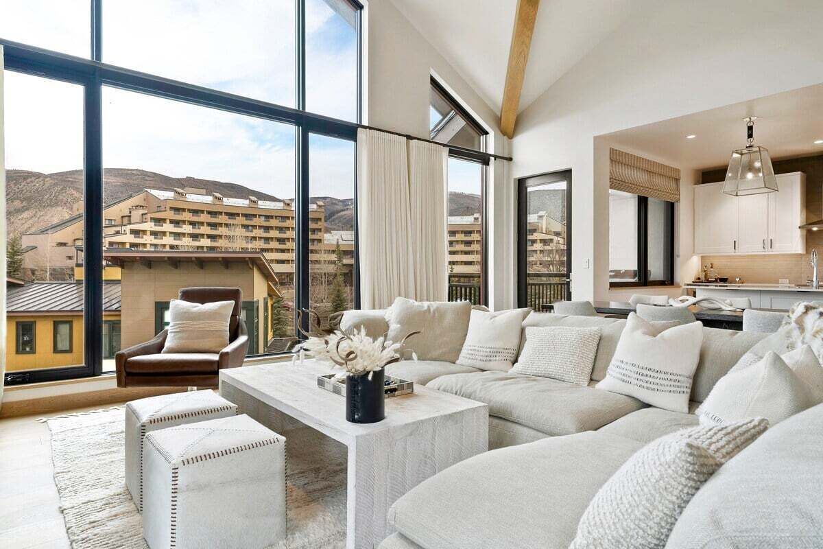 Ein modernes Wohnzimmer mit großem Fenster, einer Sofagarnitur, einem Couchtisch und Blick auf einen Gebäudekomplex.