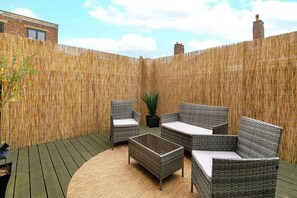 An outdoor patio with wicker furniture, a woven bamboo fence, and a view of a brick building. - Shoreditch Hoxton 2BR, 2 Bath, Terrace Sleeps 6 (Greater London)