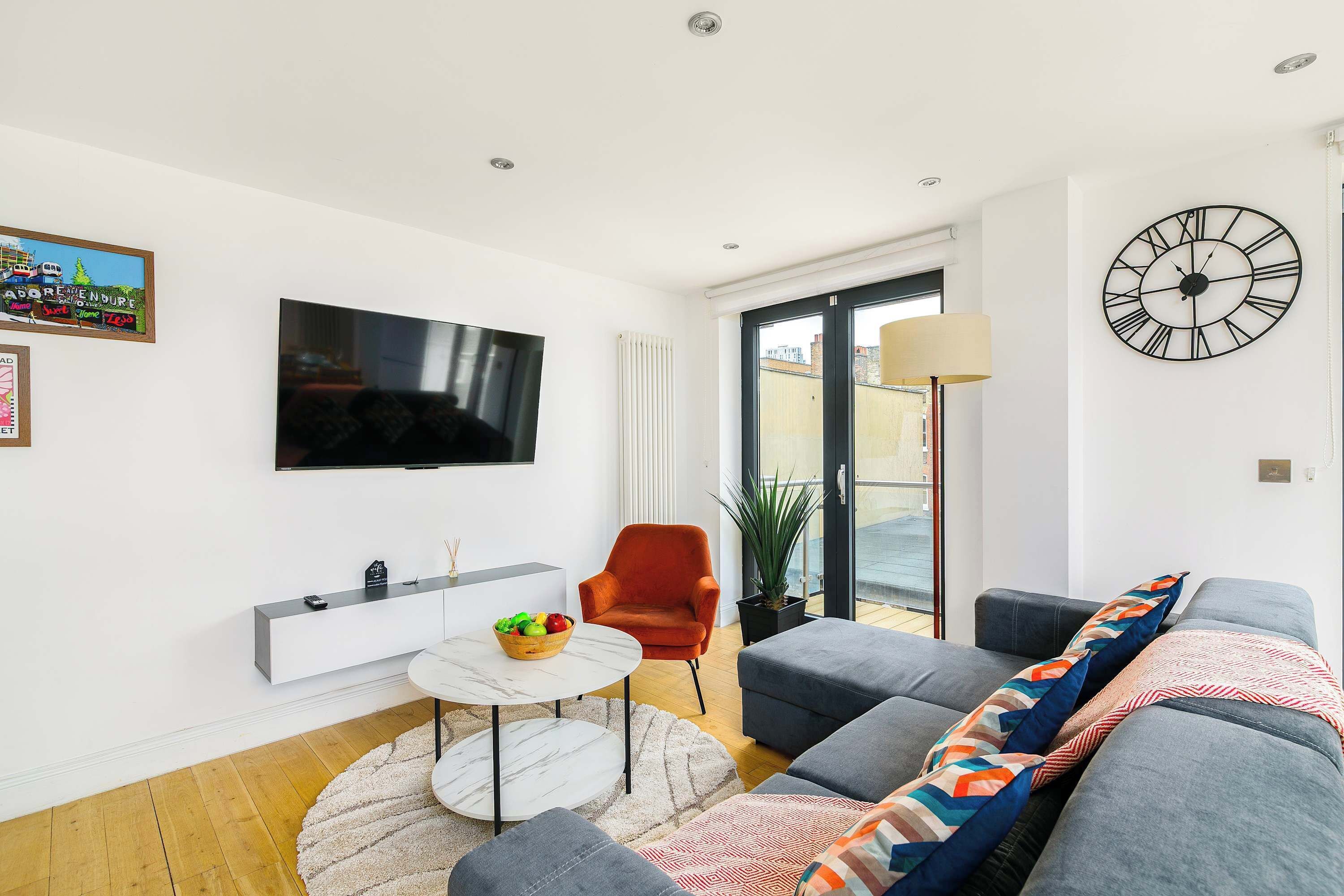 A modern living room with a flat-screen TV, a sofa, a coffee table, and a large clock on the wall.