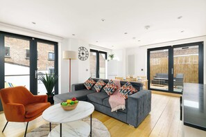 Un salón moderno con un sofá gris, un sillón naranja y una mesa redonda con un frutero.