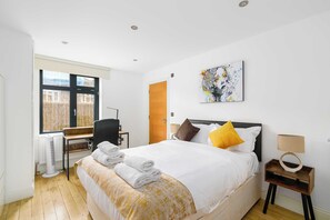 A hotel room with a bed, a desk, a chair, a window with blinds, and a painting on the wall. - Shoreditch Hoxton 2BR, 2 Bath, Terrace Sleeps 6 (Greater London)