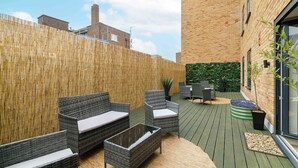 Un patio al aire libre con mobiliario de mimbre, piso verde y cerramiento de bambú.