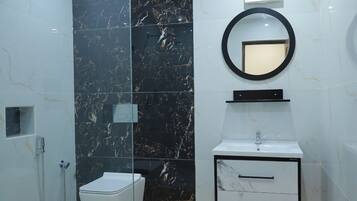 A modern bathroom with a glass shower enclosure, a marble wall, a white sink with a mirror, and a wooden floor.