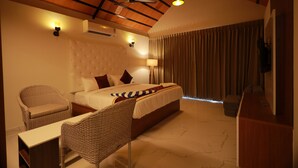 A hotel room with a bed, a chair, a desk, a ceiling fan, and a TV. - DEE COTTAGE (Nagercoil)