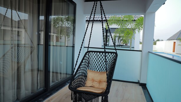 A hanging chair with a cushion on a balcony with a view of buildings and trees. - DEE COTTAGE (Nagercoil)