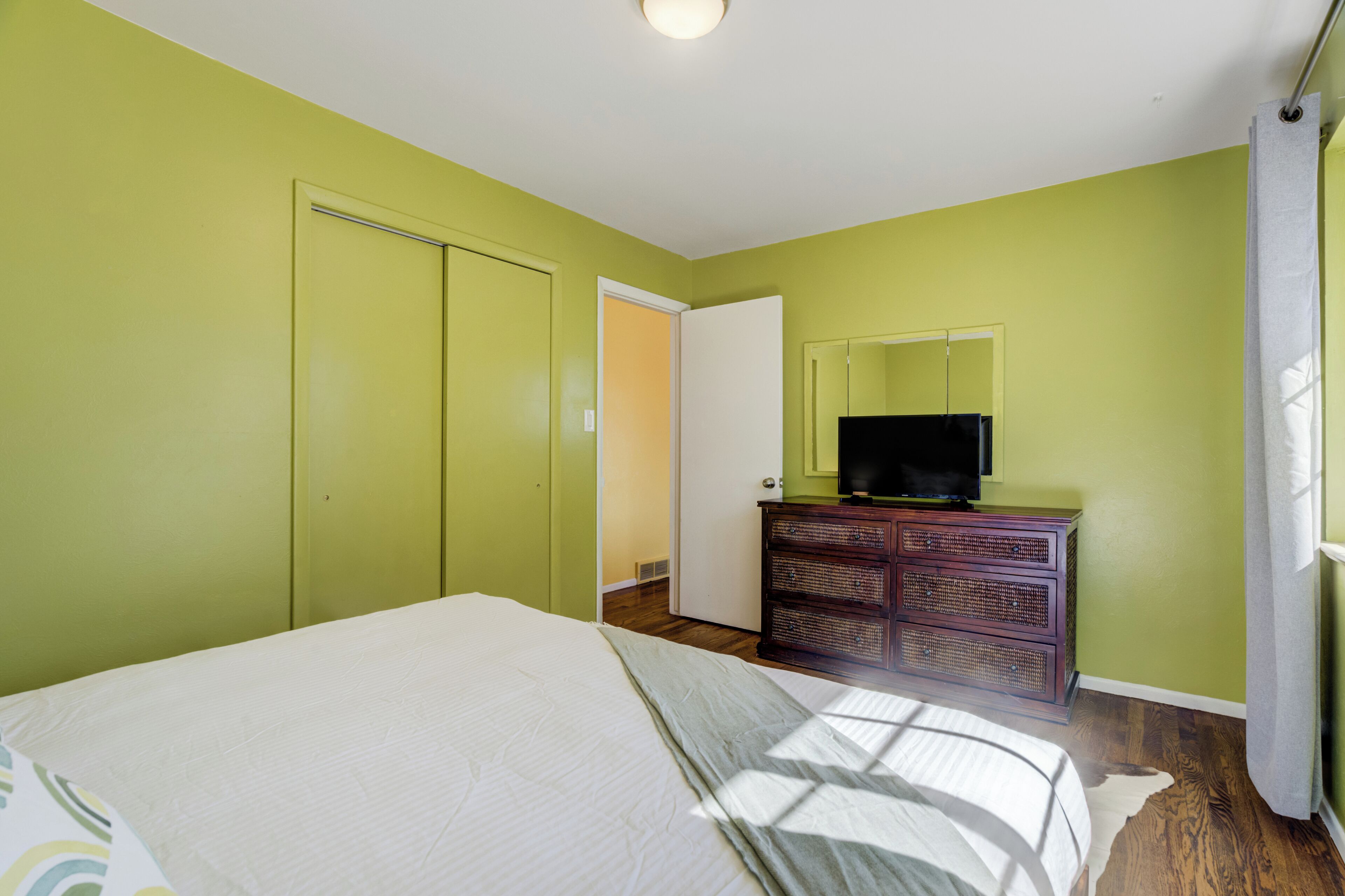 Une chambre à coucher comprenant un lit, une commode, un téléviseur et une porte donnant sur une autre pièce.