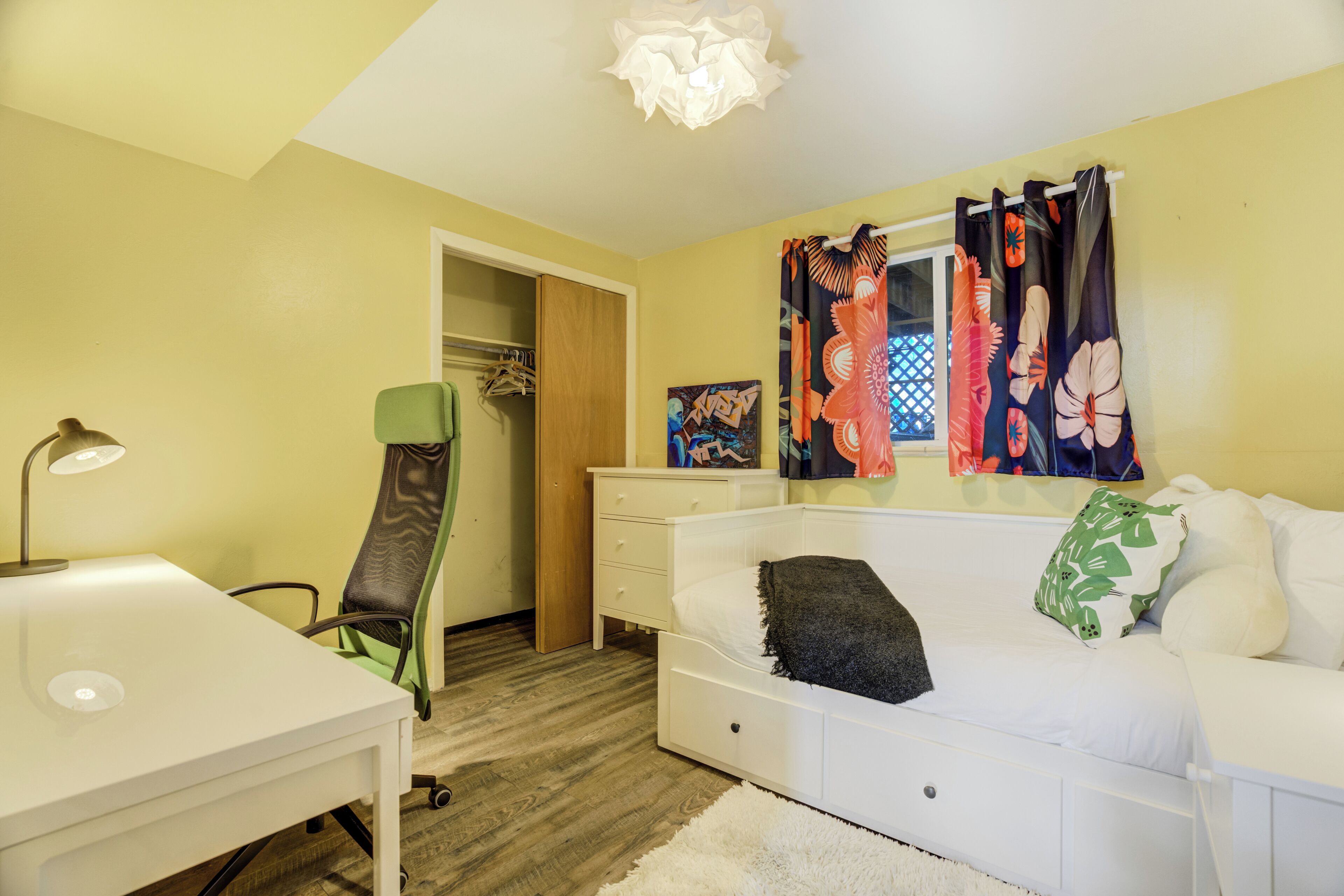 Una habitación con un escritorio blanco, una silla verde, un sofá blanco y una cama con almohada verde y blanca.