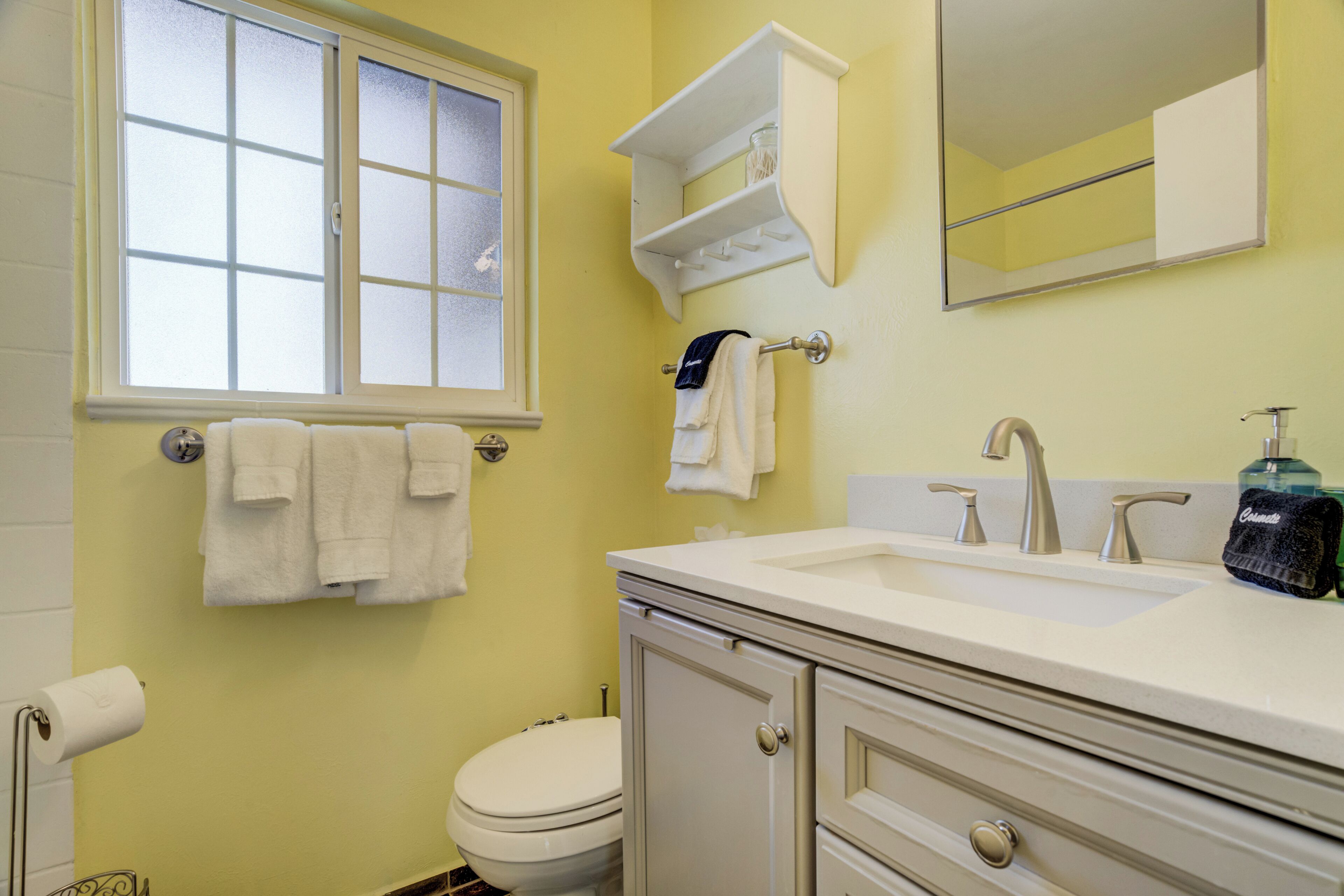 A bathroom with a toilet, sink, mirror, and towel rack.