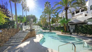 Una piscina con escalones que bajan hacia ella, rodeada de palmeras y un muro de piedra.