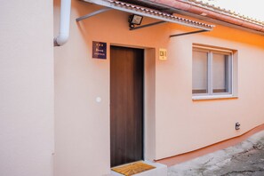 A single-story building with a wooden door and a window. There are two signs: one indicating the building is an apartment and another with a number.