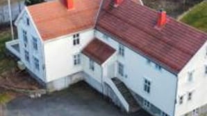 En stor, hvid bygning med rødt tag, en midterindgang og en lille tilbygning.