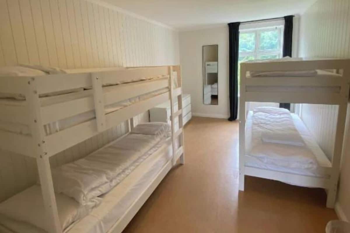 Habitació amb dos llits superposats, terres de fusta, una finestra amb cortines i un mirall a la paret.