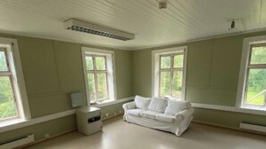 En rummelig stue med en hvid sofa, store vinduer og en ventilator.