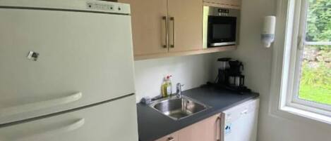 A compact kitchen with a refrigerator, microwave, sink, and a window providing a view of greenery outside.