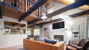 Ein geräumiges Wohnzimmer mit Holzboden, einer Couch, einem Kamin und einem Essbereich.