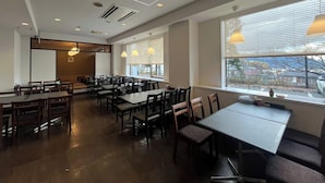 A spacious dining area with multiple tables and chairs, large windows with blinds, and pendant lighting. - Fuji Premium Hotel (Fujiyoshida)