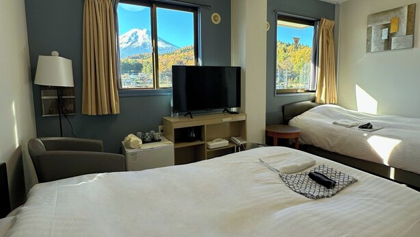 A hotel room with two beds, a TV, a desk, and a view of a mountain. - Fuji Premium Hotel (Fujiyoshida)