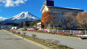 A hotel with a view of a snow-capped mountain, a parking lot, and a street with autumn trees. - Fuji Premium Hotel (Fujiyoshida)