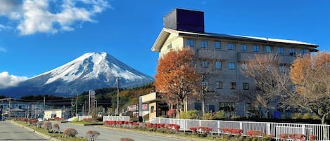 A hotel with a view of a snow-capped mountain, a parking lot, and a street with autumn trees.