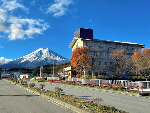 Un albergo con vista su una montagna innevata, un parcheggio e una strada alberata d'autunno.